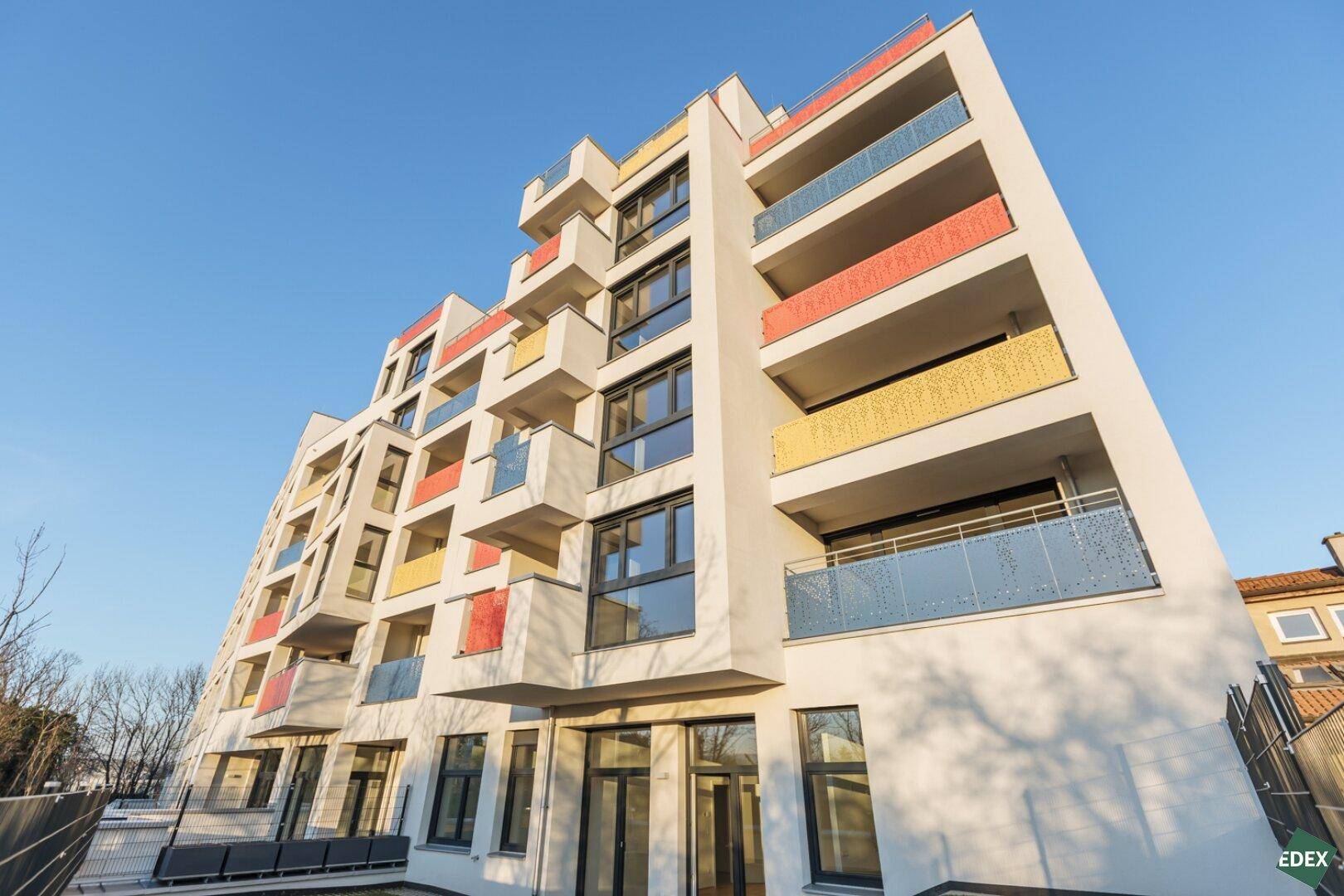 Neubau-Wohngebäude mit gestuften Balkonen und farbigen Akzenten unter strahlend blauem Himmel.