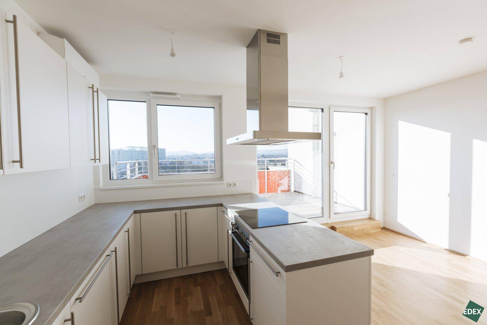 Helle, moderne Küche mit weißen Schränken, Kochinsel und Fenster mit Blick auf die Stadtlandschaft.