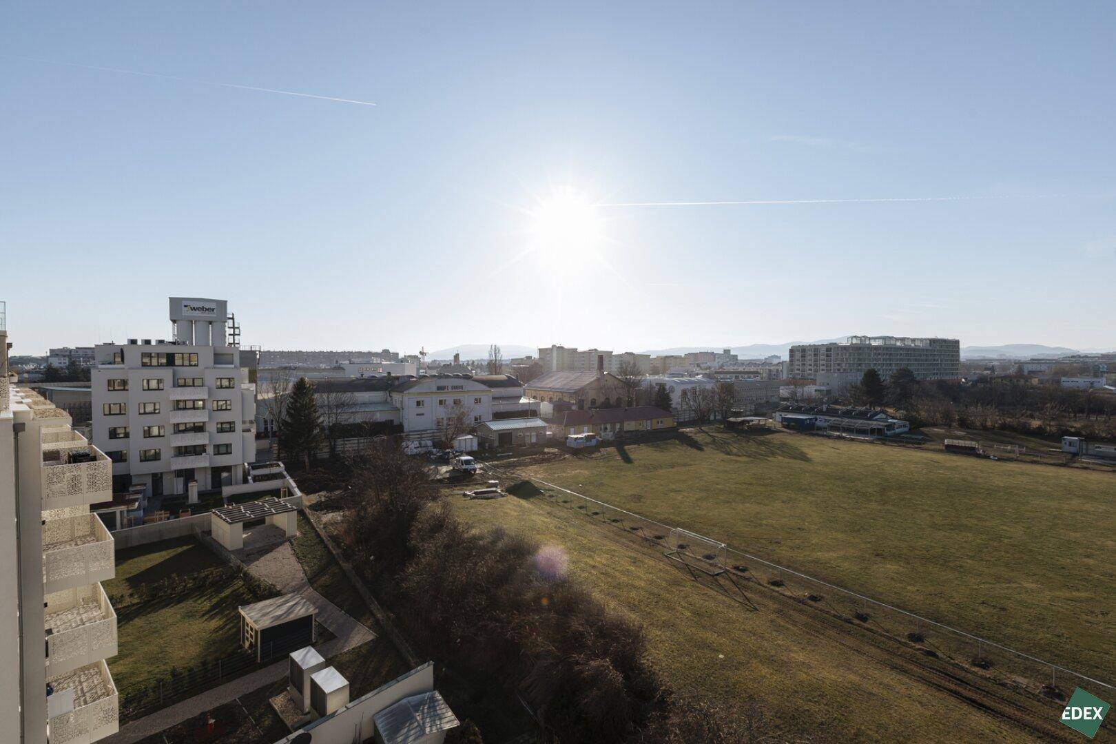 Panoramablick über eine Stadt mit weiten Grünflächen und Gebäuden unter einem strahlend blauen Himmel.