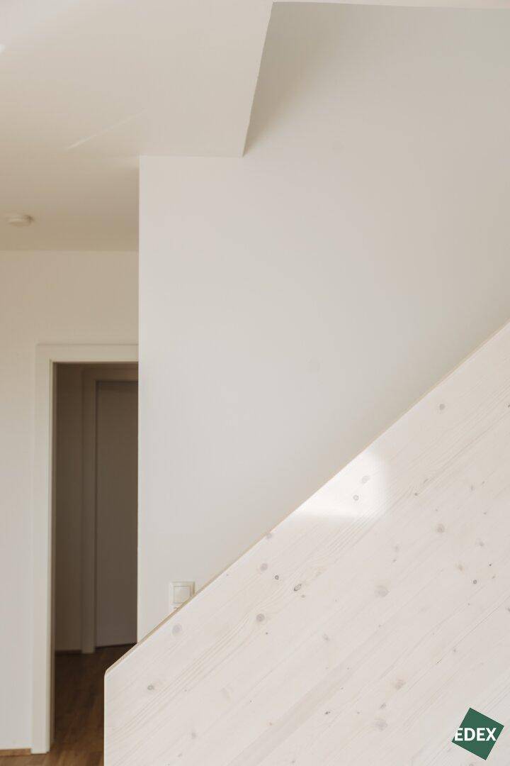 Detailansicht einer weißen Wand und einer hellen Holztreppenkonstruktion, die nach oben führt.