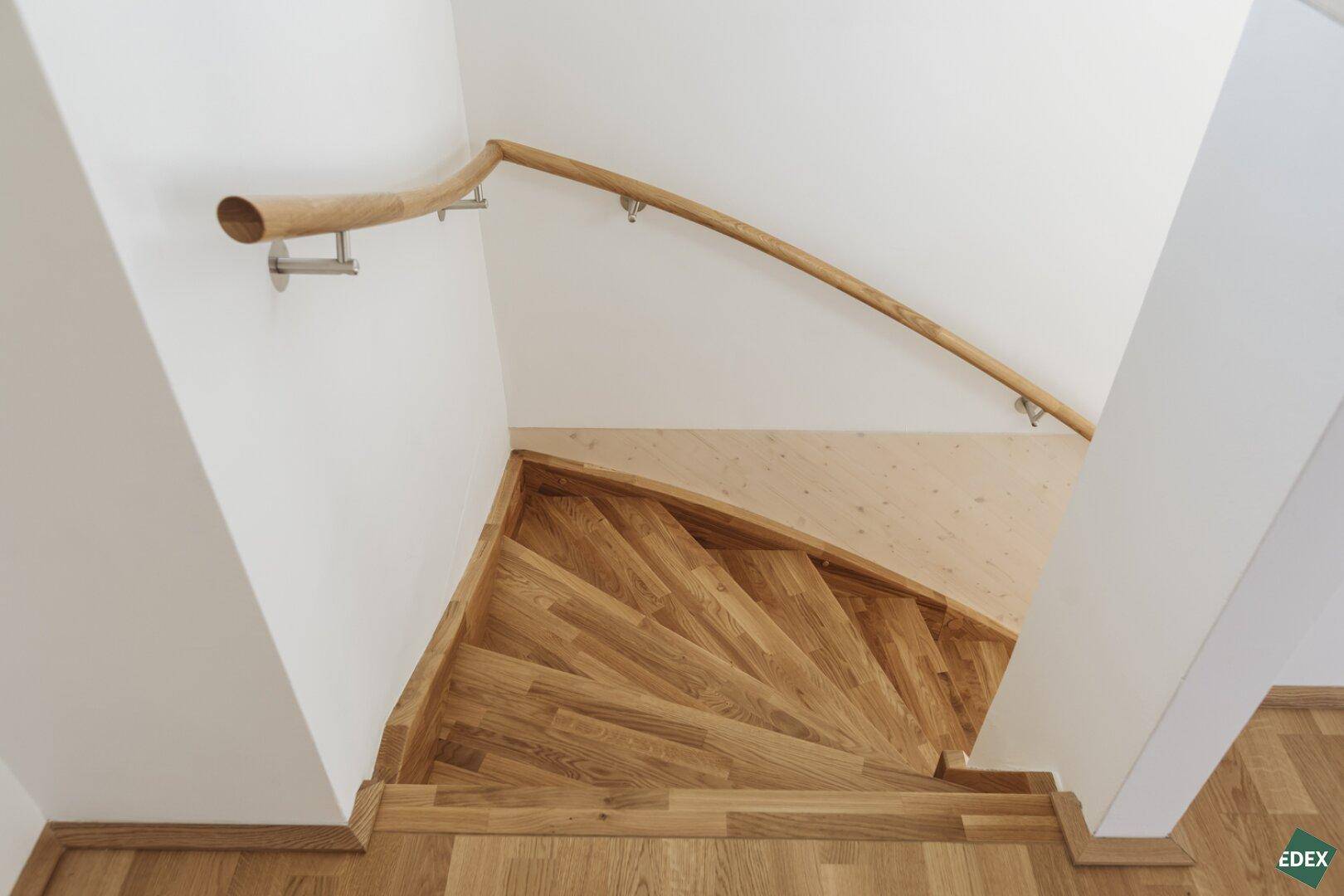 Blick von oben auf eine geschwungene Holztreppe mit passendem Handlauf in einem hellen Treppenhaus.