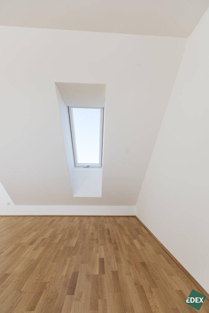 Heller Raum im Dachgeschoss mit schrägem Dachfenster und Holzboden, ideal für ein Schlafzimmer oder Büro.
