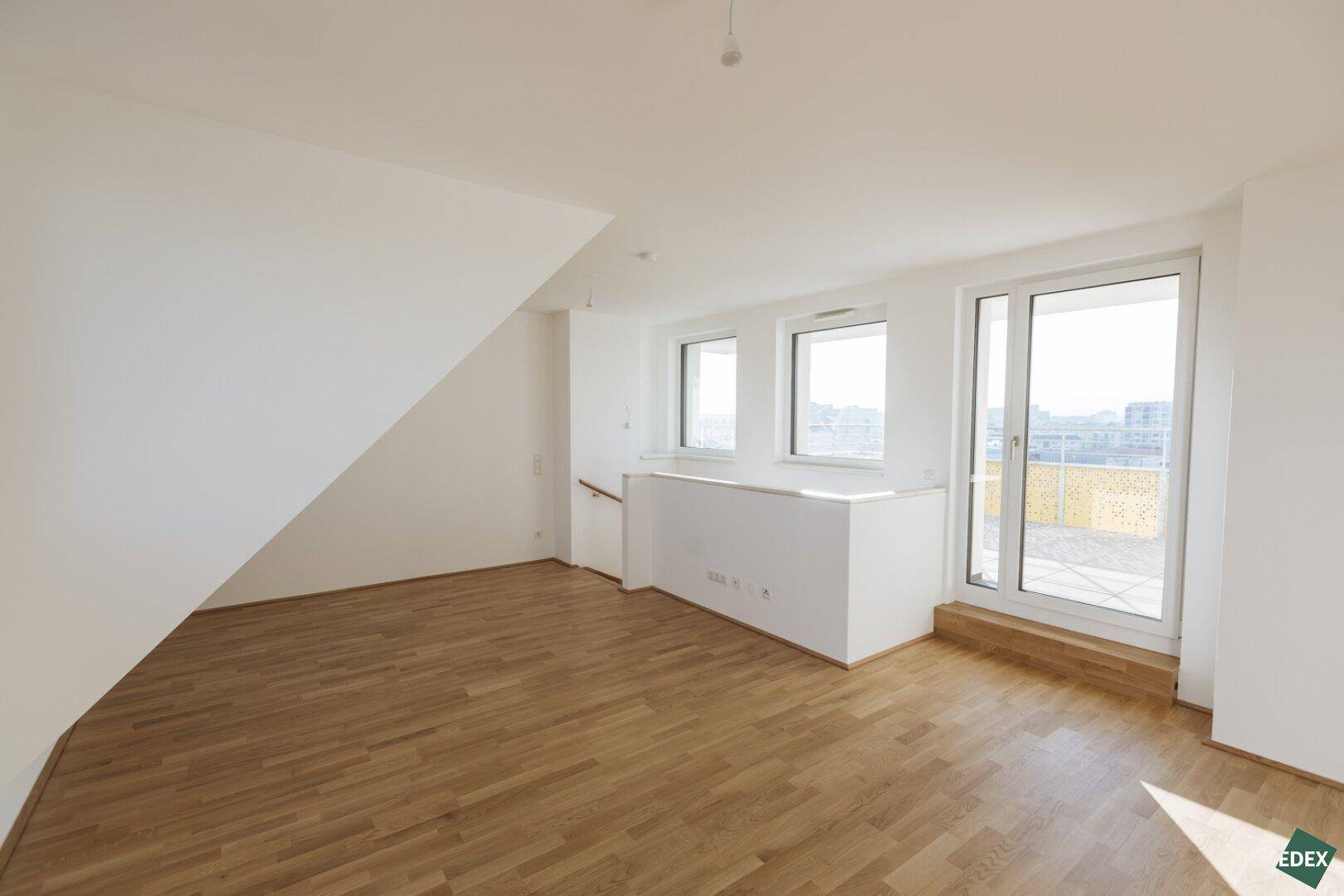 Geräumiger Dachgeschossraum mit großen Fenstern und Zugang zu einem Balkon, bietet viel Tageslicht.