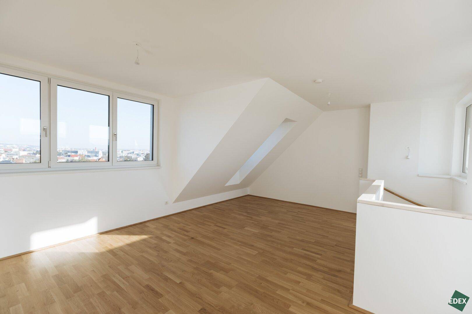 Helles Dachgeschosszimmer mit mehreren Fenstern und schrägen Wänden, bietet einen weiten Ausblick.