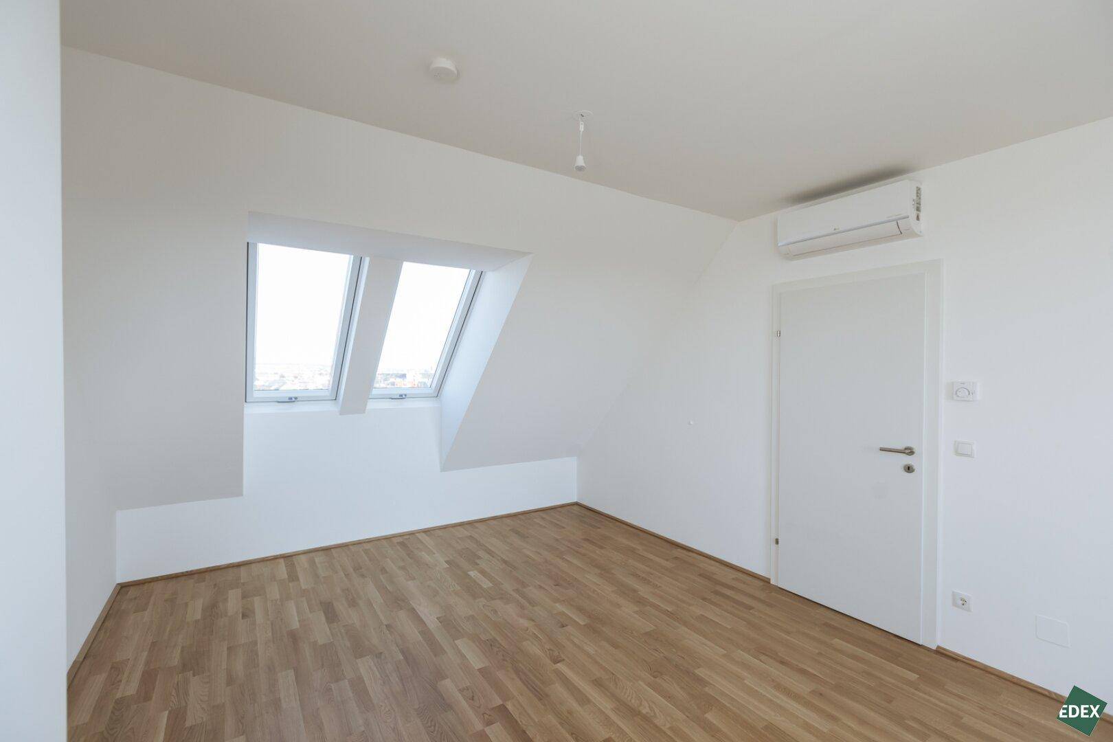 Dachgeschossraum mit zwei Dachfenstern, Holzboden und Klimaanlage, ideal für ein Schlafzimmer.