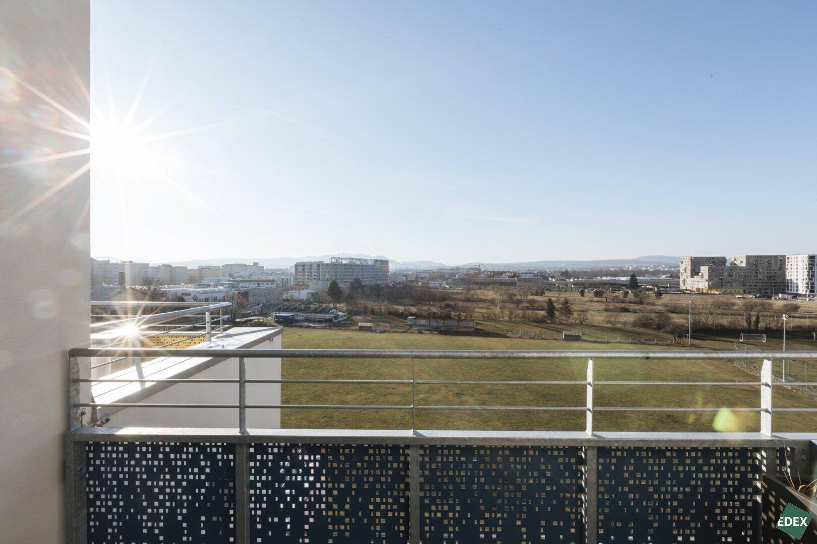 Heller Balkon mit sonnigem Ausblick auf die Stadt und die Umgebung, umgeben von einer modernen Brüstung.