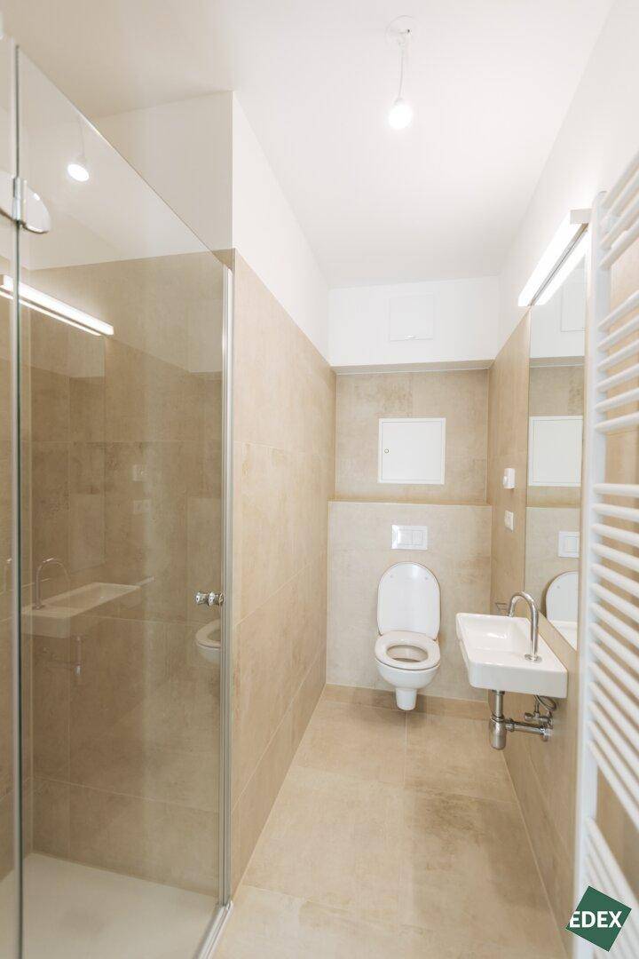 Modernes Badezimmer mit beigefarbenen Fliesen, Dusche und wandhängendem WC, ausgestattet mit Handtuchheizkörper.