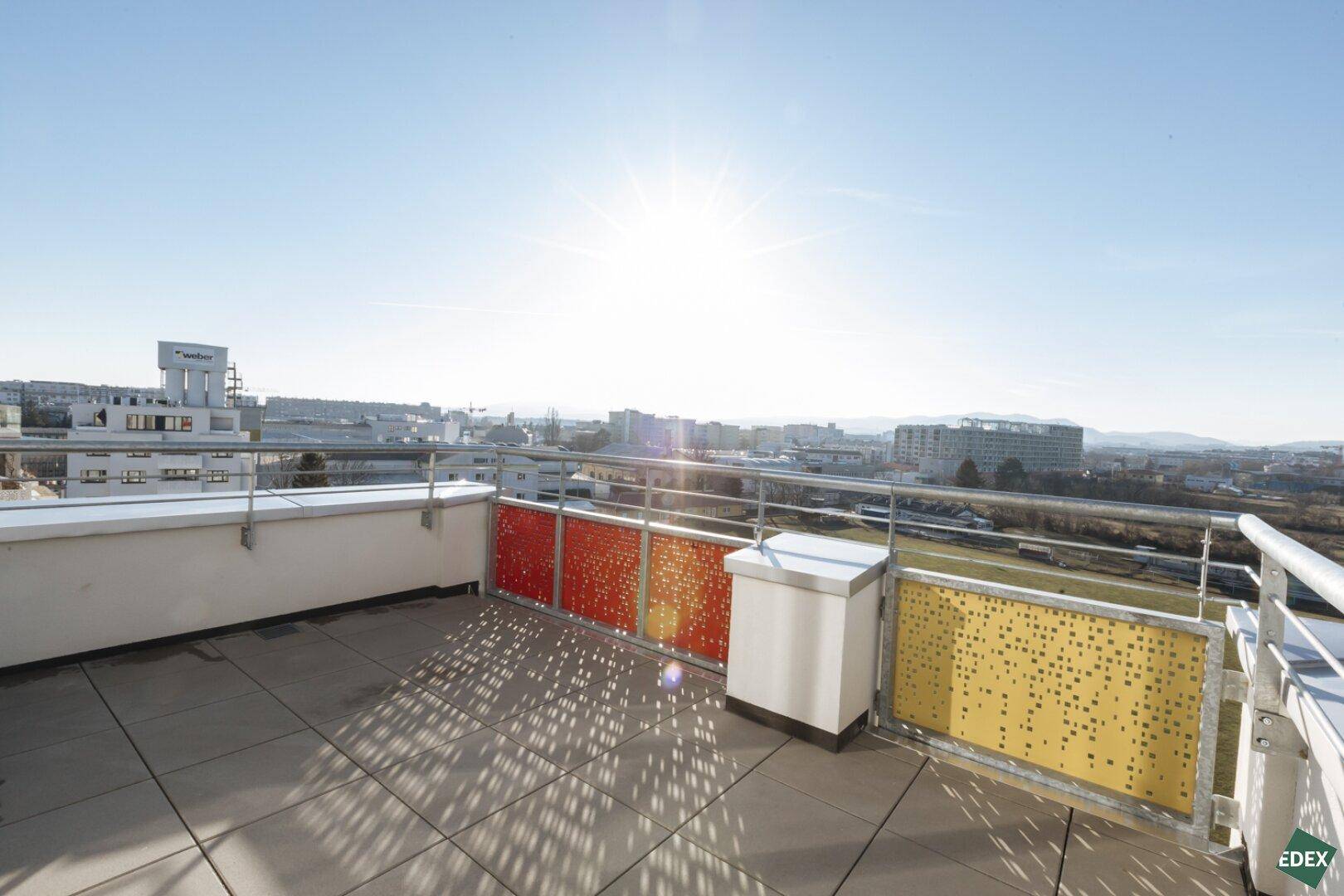 Große Dachterrasse mit farbigen Paneelen und weitem Blick über die Stadt, ideal für Sonnenbäder.