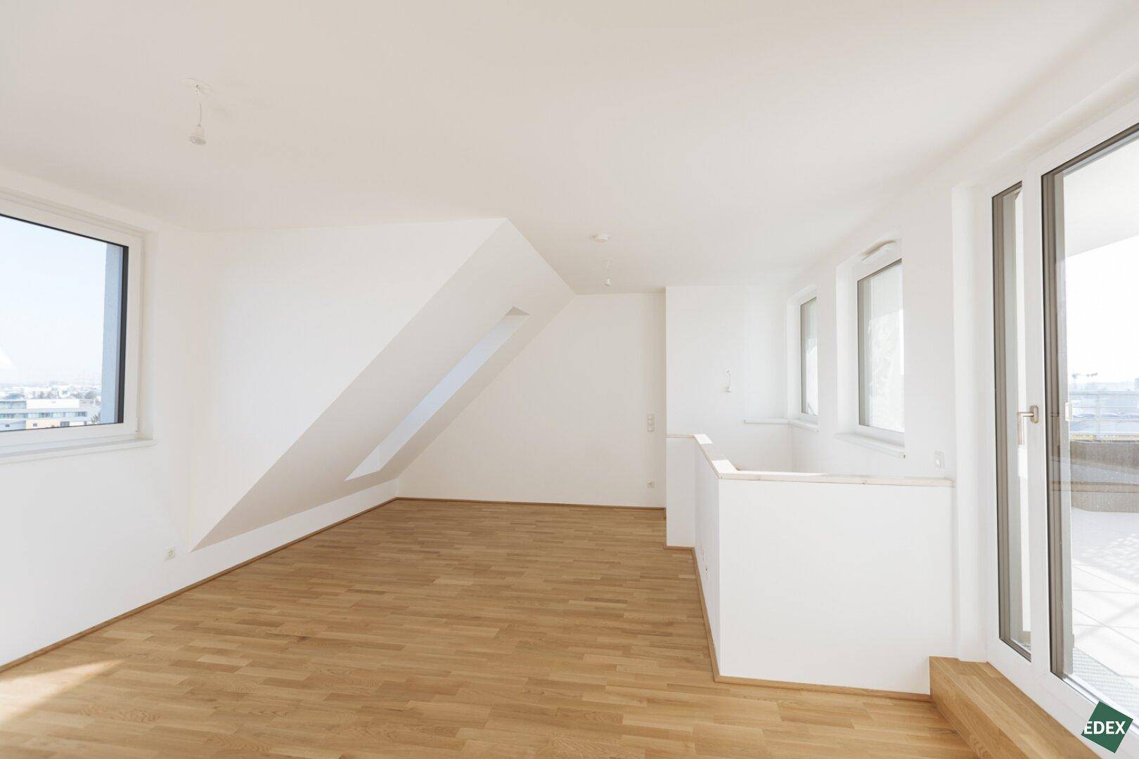 Geräumiger Dachgeschossraum mit großen Fenstern und Zugang zu einem Balkon, bietet viel Tageslicht.