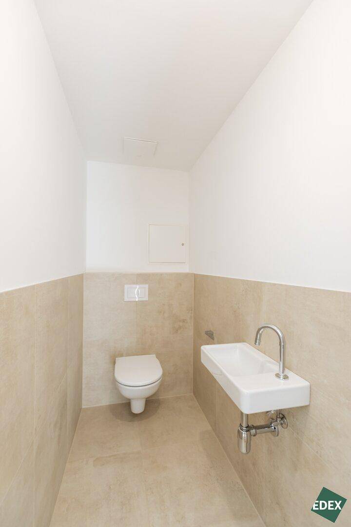 Modernes Gäste-WC mit beigefarbenen Fliesen, wandhängendem WC und kleinem Waschbecken.