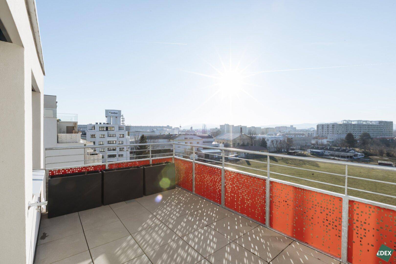 Sonnige Dachterrasse mit modernem Geländer und weitem Blick über die Stadt und grüne Flächen.