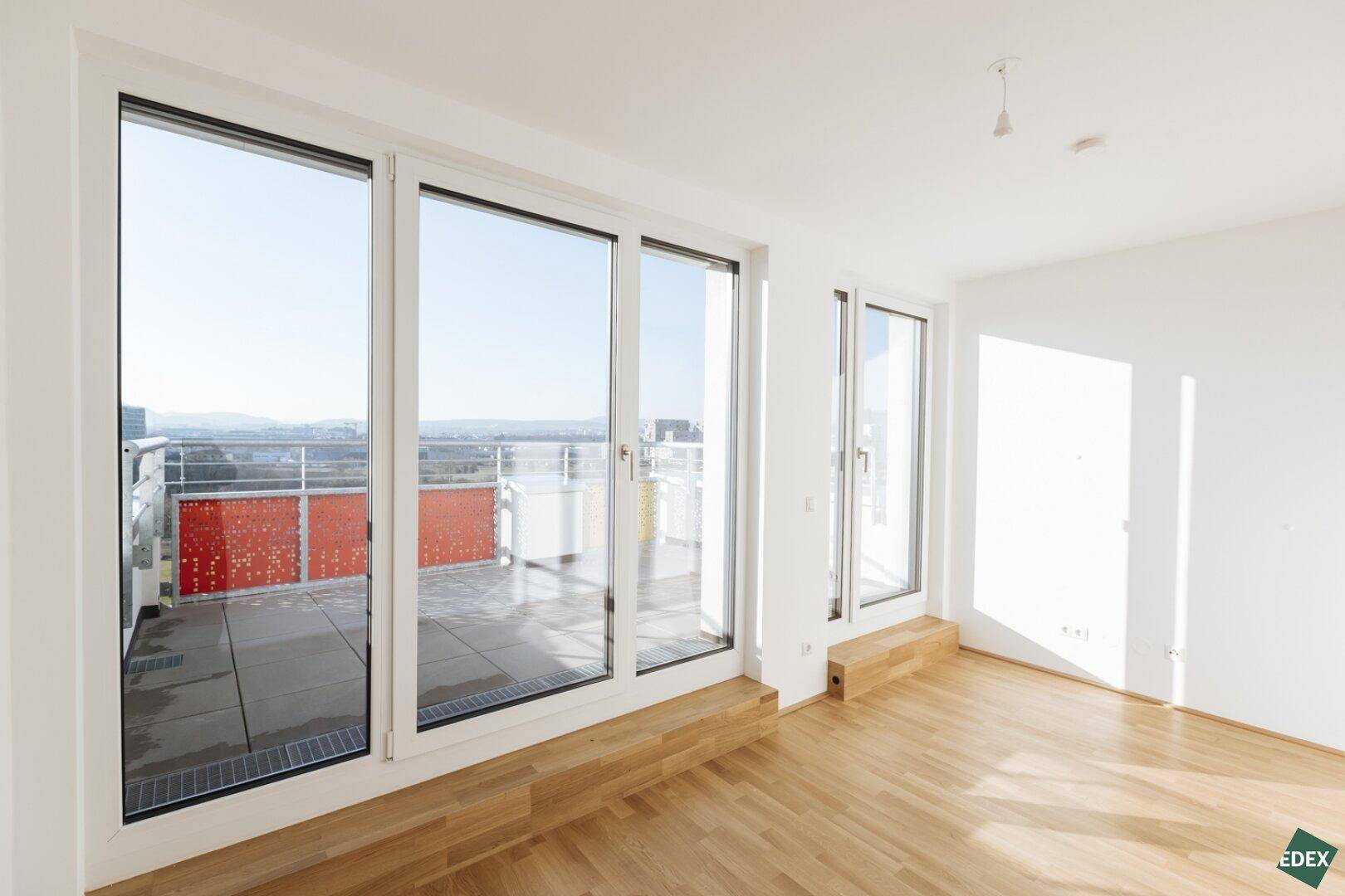 Lichtdurchfluteter Wohnraum mit großen Fenstern und Zugang zu einem sonnigen Balkon.