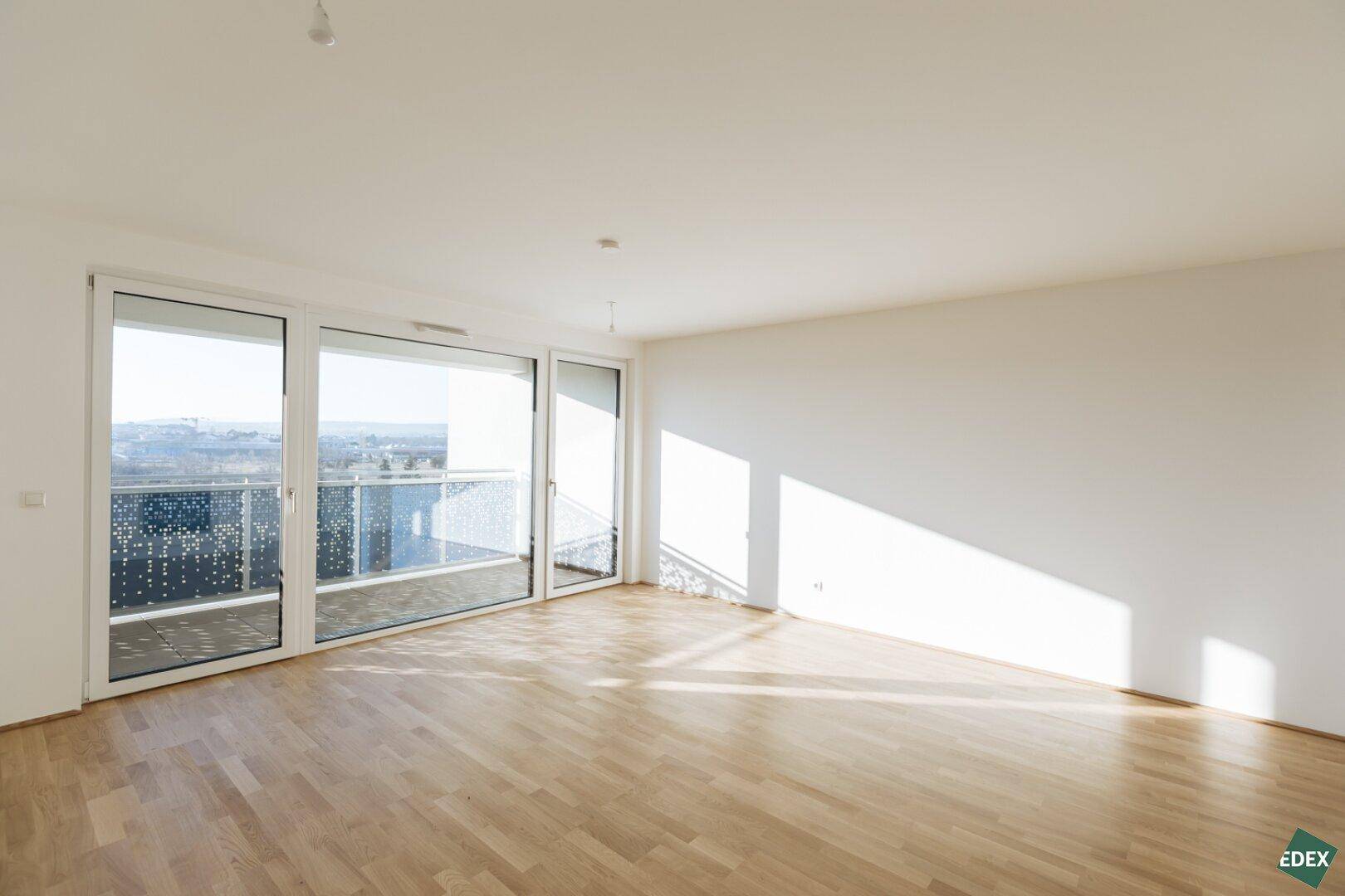 Geräumiger Wohnbereich mit hellem Parkettboden und großen Schiebetüren zum Balkon.