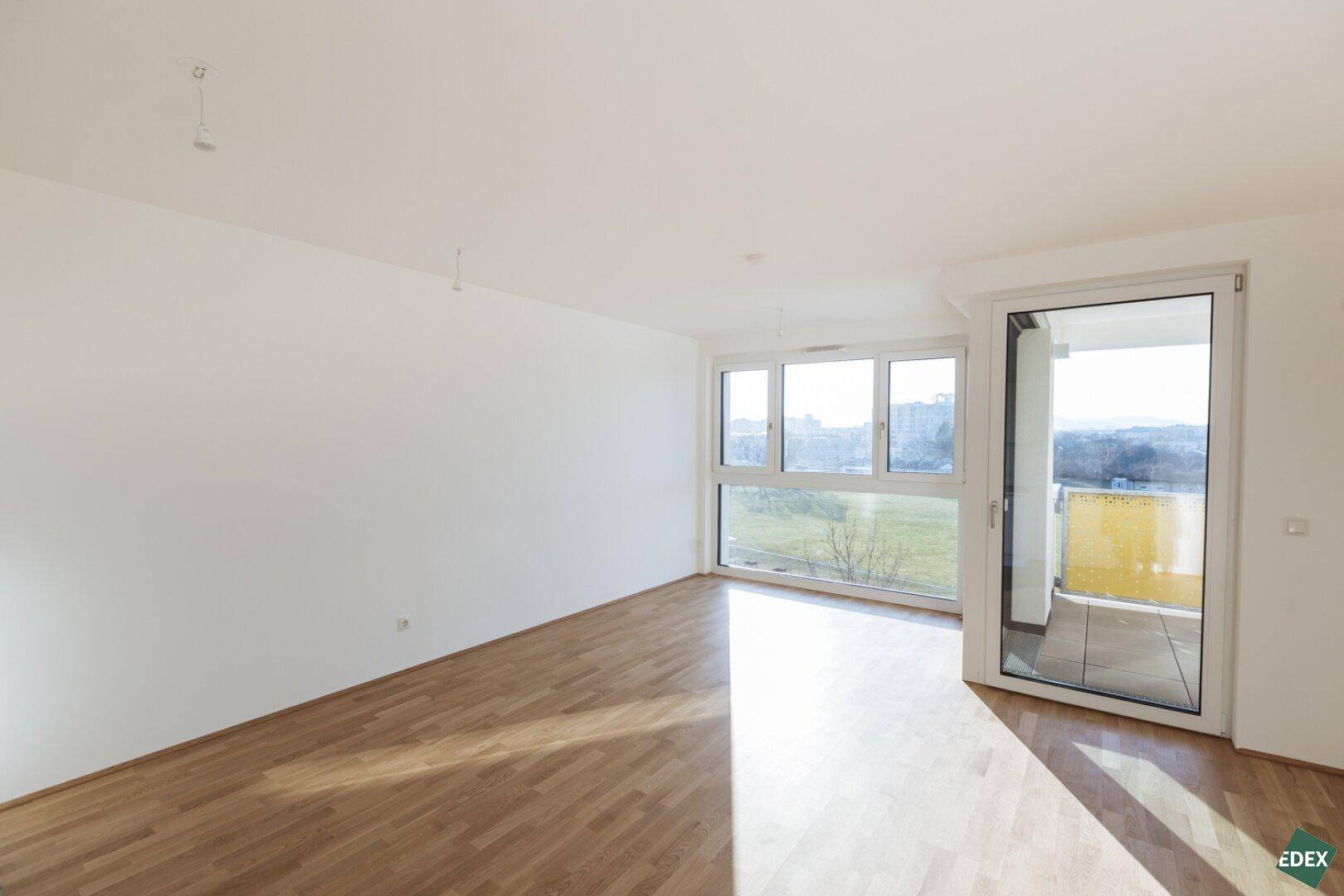 Heller Wohnraum mit Parkettboden, großen Fenstern und direktem Zugang zum Balkon.