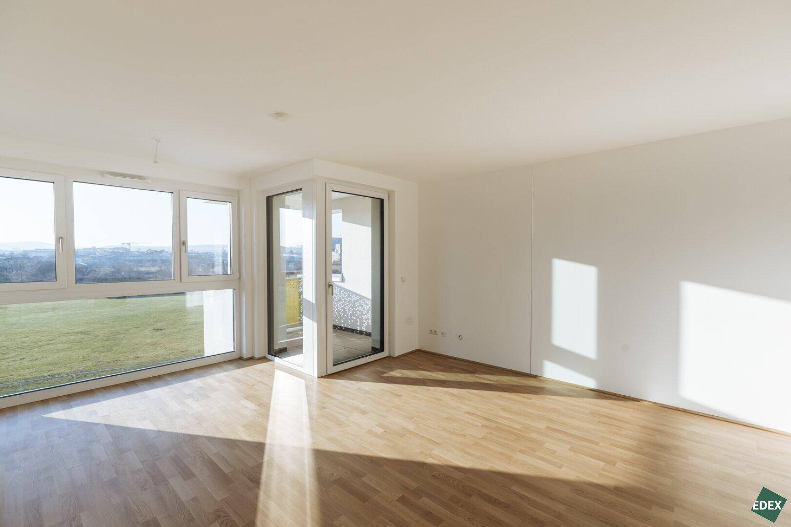 Lichtdurchfluteter Wohnbereich mit Eckfenstern, Parkettboden und Zugang zum Balkon.
