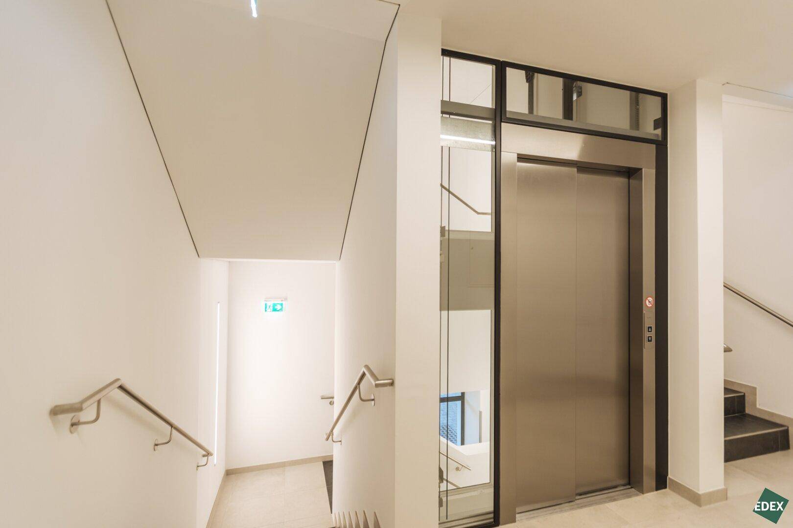 Heller Treppenaufgang mit modernem Aufzug und Handläufen in einem Mehrfamilienhaus.