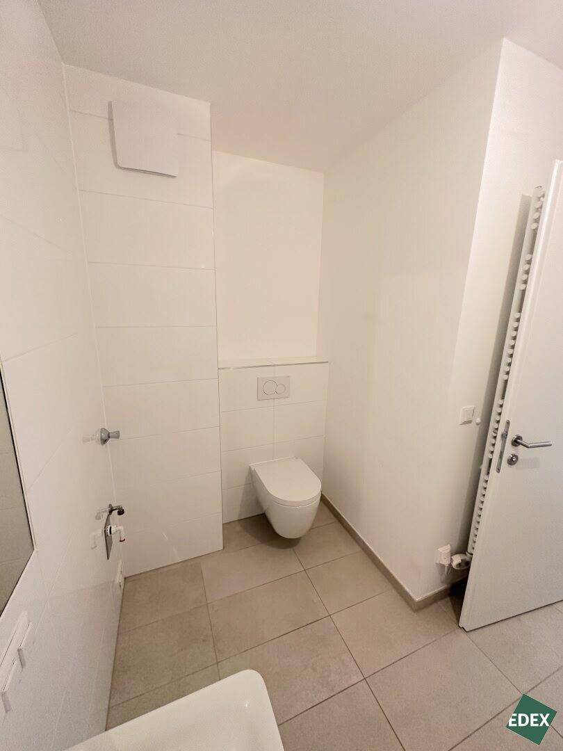 Separates WC mit wandhängender Toilette, Fliesenboden und Handtuchheizkörper.