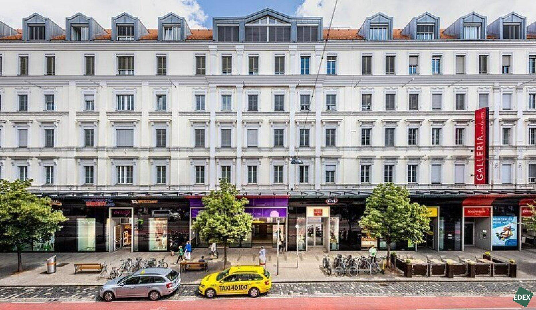 Historisches Gebäude mit vielen Fenstern und Geschäften im Erdgeschoss, belebte Straße davor.