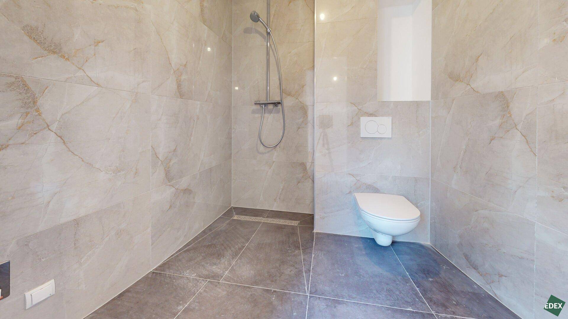 Modernes Badezimmer mit großformatigen Fliesen, ebenerdiger Dusche und wandhängendem WC.