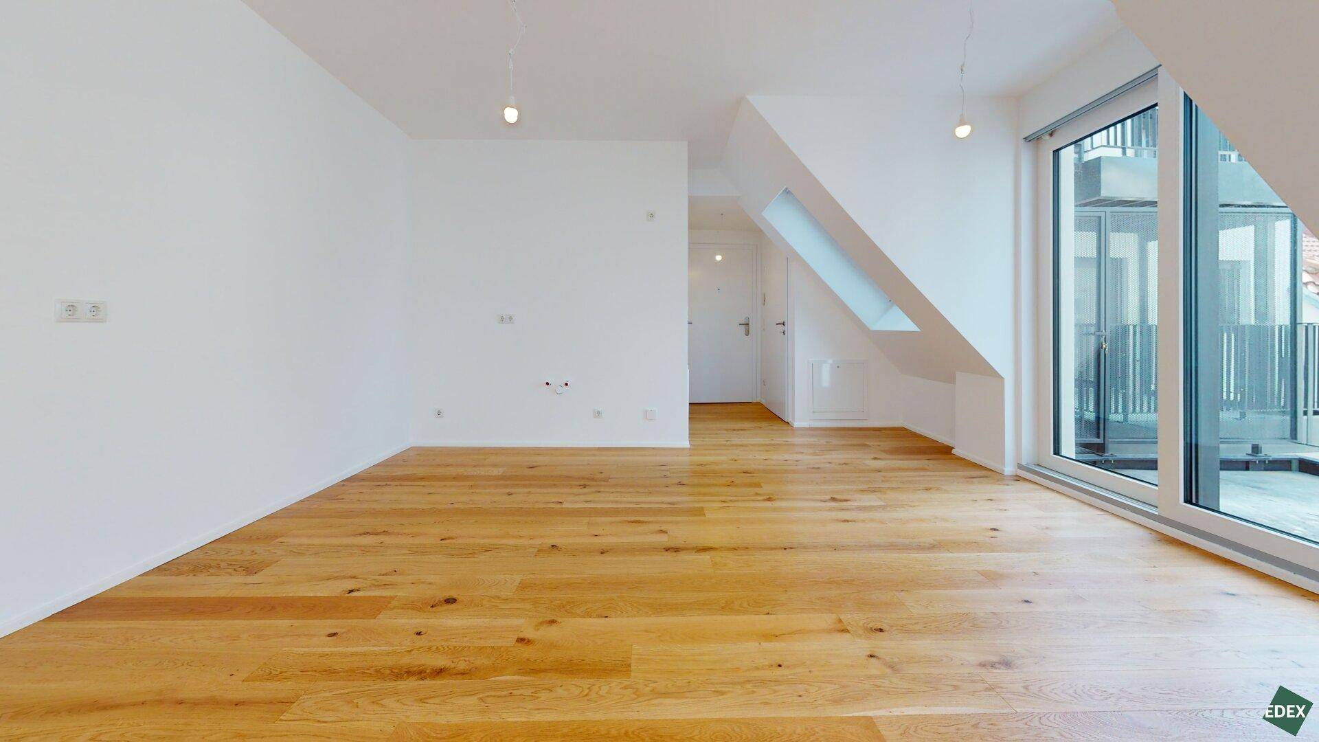 Heller Raum mit Holzboden und großer Glasfront, die zu einem Außenbereich führt.