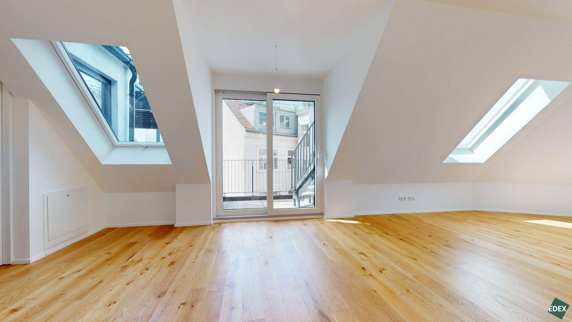 Heller Wohn- und Essbereich im Dachgeschoss mit Holzboden, Dachfenstern und Zugang zum Balkon.