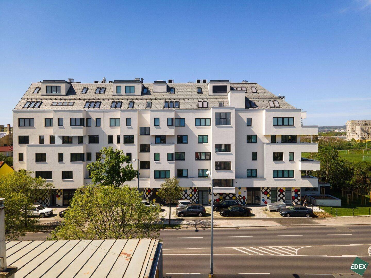Ansicht der modernen Wohnanlage von der Straße mit Parkplätzen und Dachfenstern.