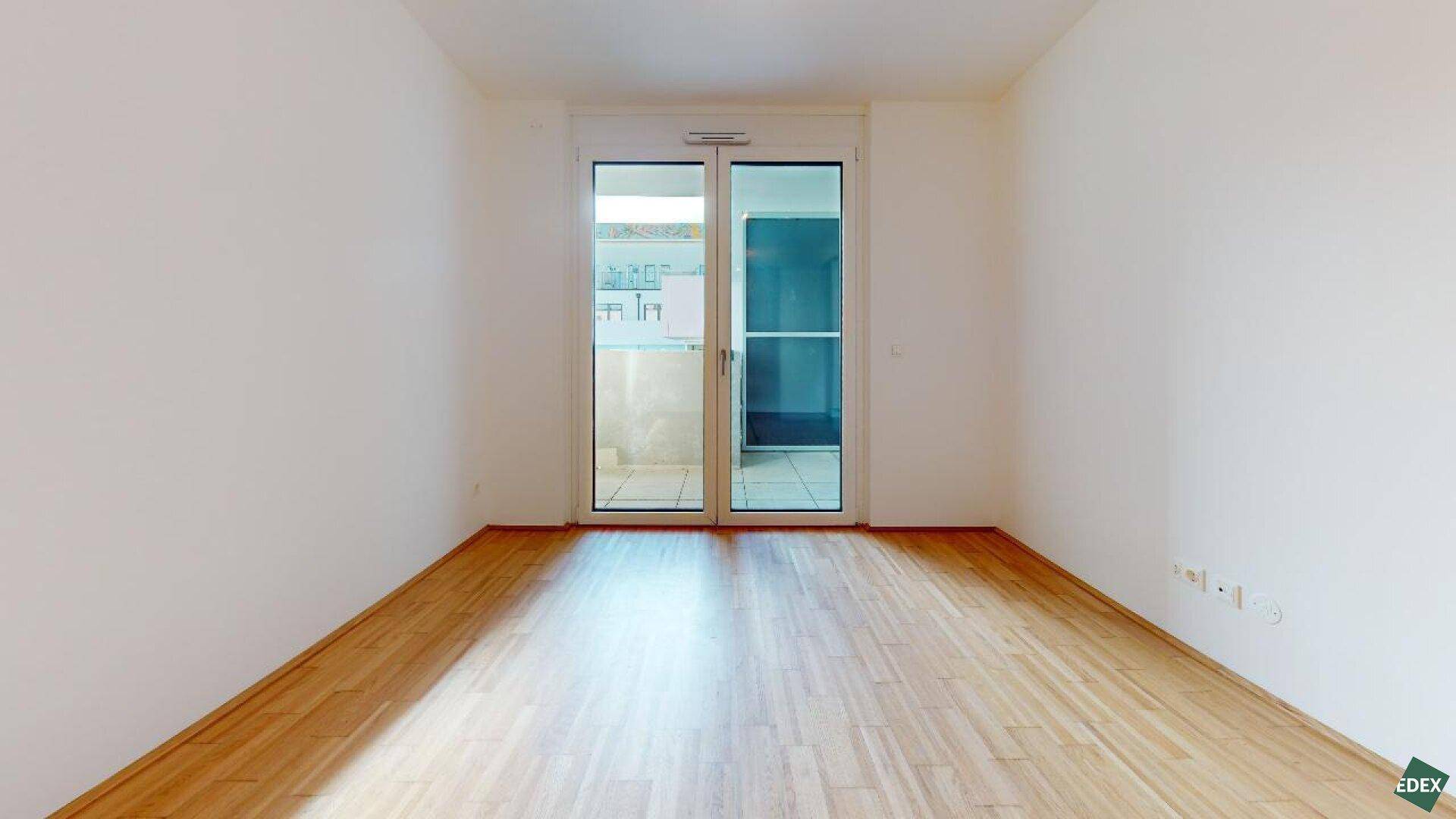 Helles Schlafzimmer mit Parkettboden und großem Fenster zum Balkon.