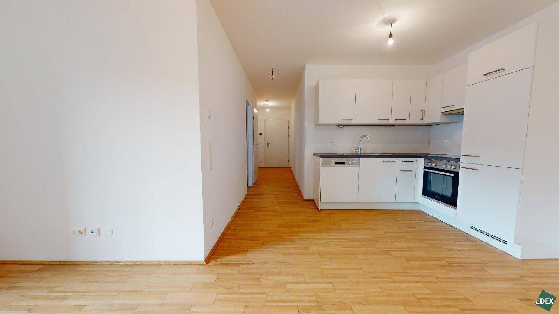 Funktionale Küchenzeile mit weißen Fronten und Blick in den angrenzenden Flurbereich.