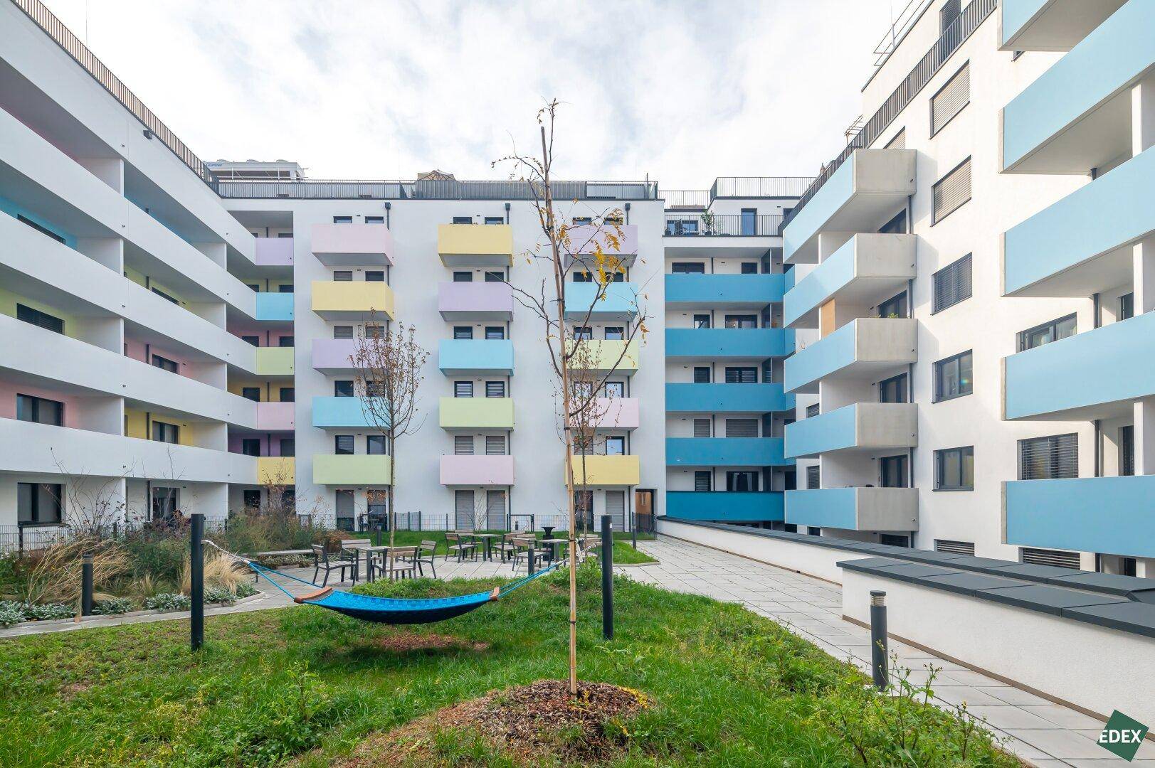 Moderner Innenhof einer Wohnanlage mit bunten Balkonen und einer Hängematte.