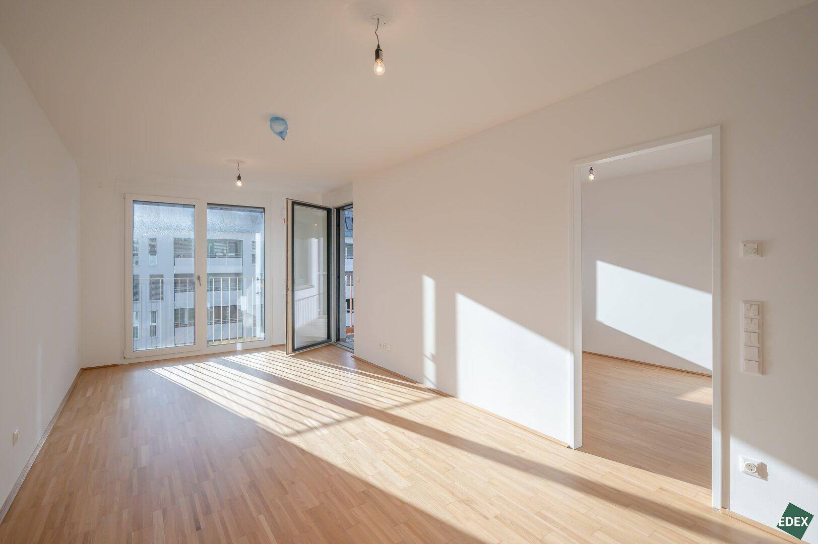 Lichtdurchfluteter Wohnraum mit Holzboden und Zugang zu einem Balkon oder einer Loggia.