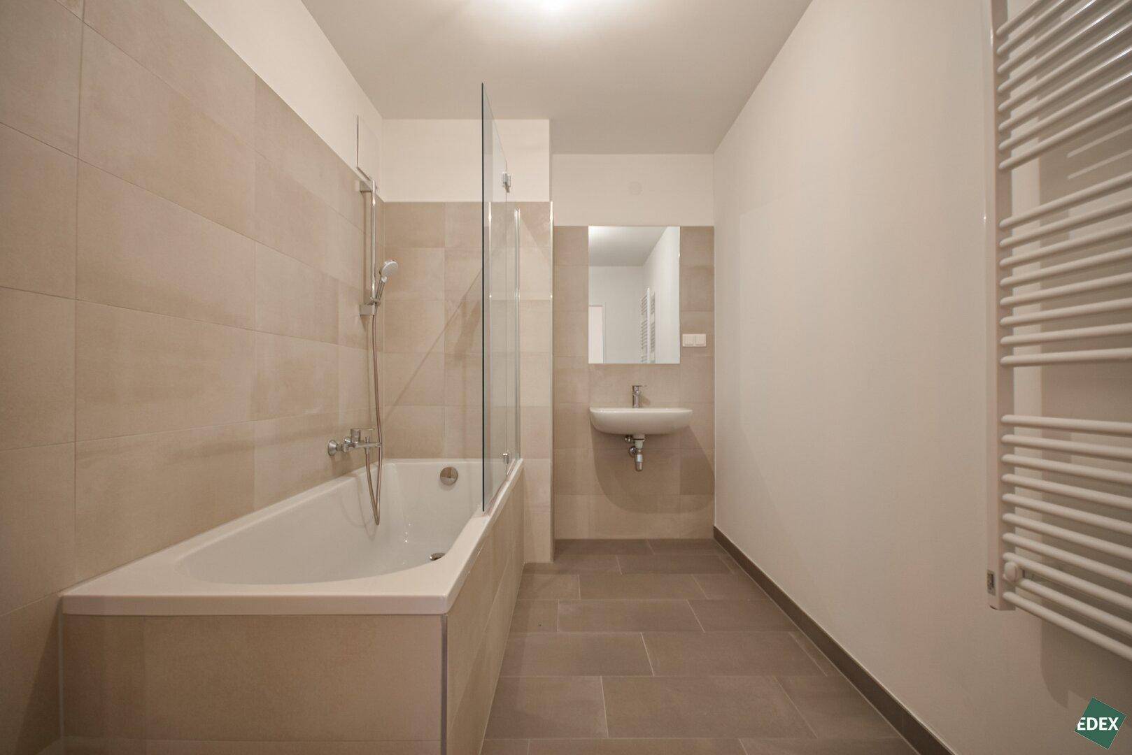 Modernes Badezimmer mit beigefarbenen Fliesen, Badewanne und beheiztem Handtuchhalter.