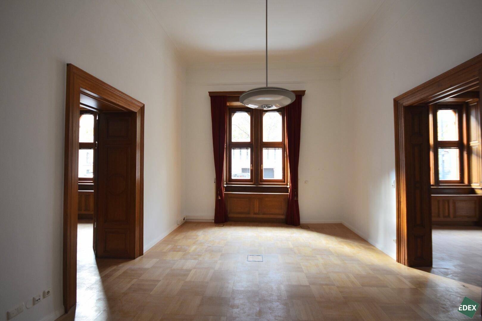 Heller, leerer Raum mit Parkettboden und zwei großen Holztüren, die den Durchgang ermöglichen.
