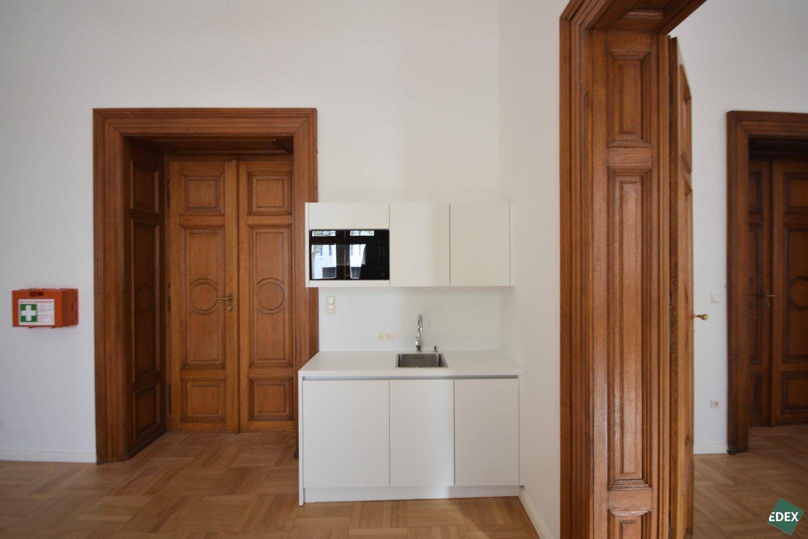 Kleine, moderne Küchenzeile mit weißen Schränken und Spüle in einem Raum mit Parkettboden.