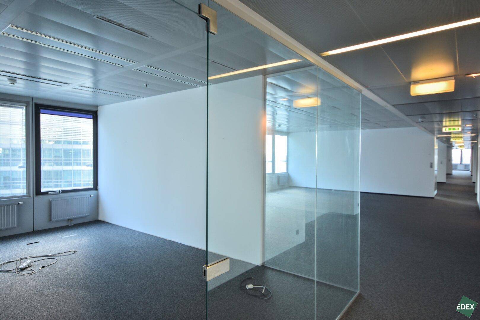 Moderner Bürobereich mit Glaswänden, Teppichboden und abgehängter Decke, schafft helle und flexible Arbeitsräume.