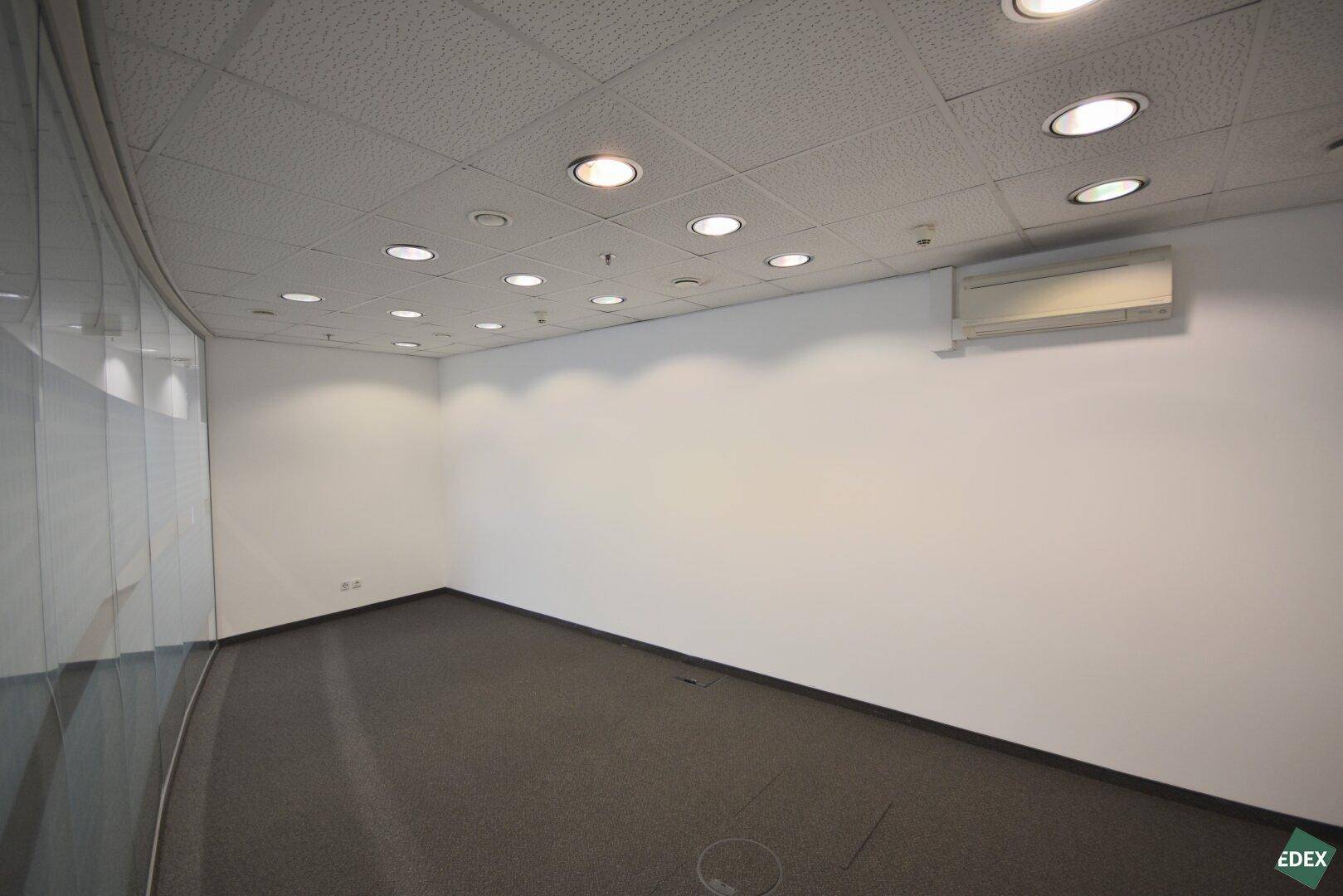 Kleinerer Bürobereich mit grauem Teppichboden, Glaswand und Klimaanlage an der Decke.