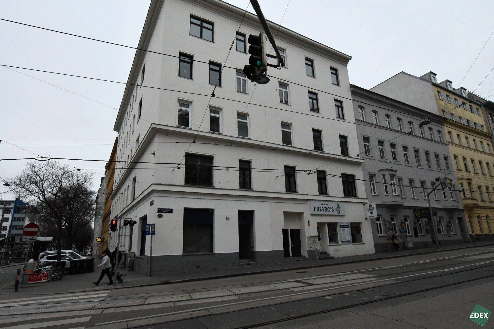 Weißes Eckgebäude mit klassischer Architektur an einer belebten Straße in der Stadt.