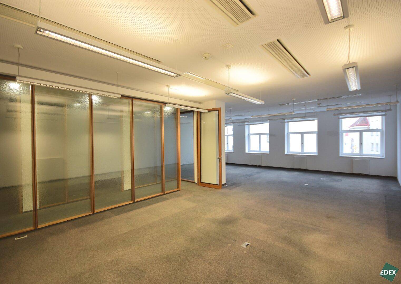Großer Bürobereich mit Teppichboden und Glaswänden, bietet viel Platz und natürliches Licht.