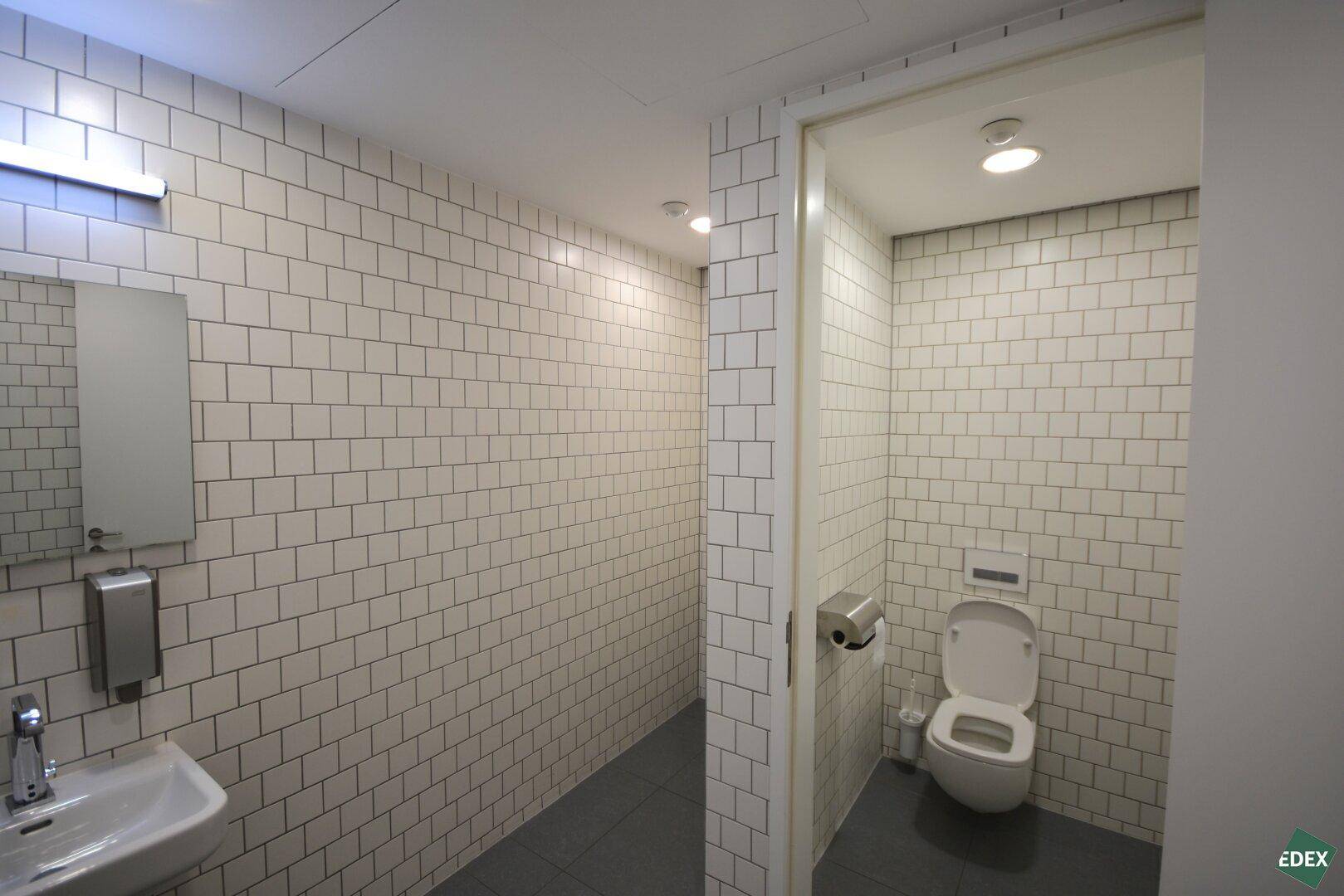 Sauberer Toilettenbereich mit weißen Fliesen und modernem Waschbecken, gut gepflegt und funktional.