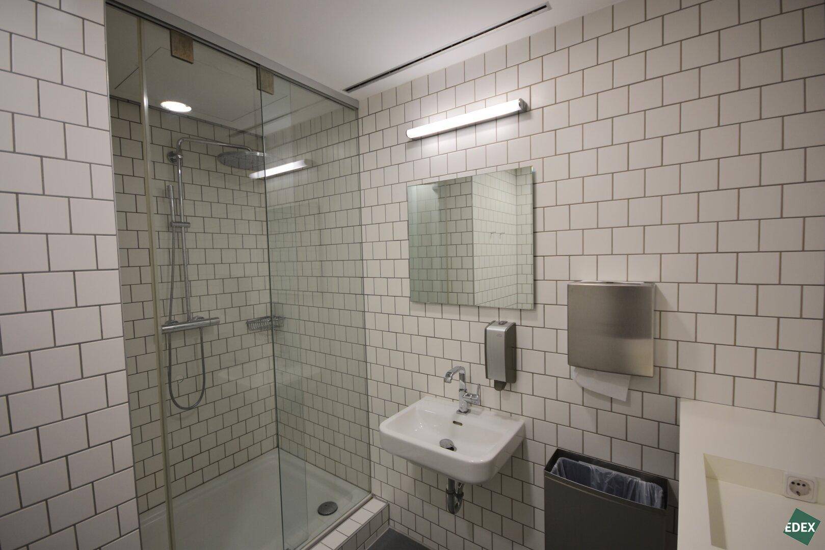 Modernes Badezimmer mit Duschkabine und weißen Fliesen, ausgestattet mit einem Waschbecken und Spiegel.