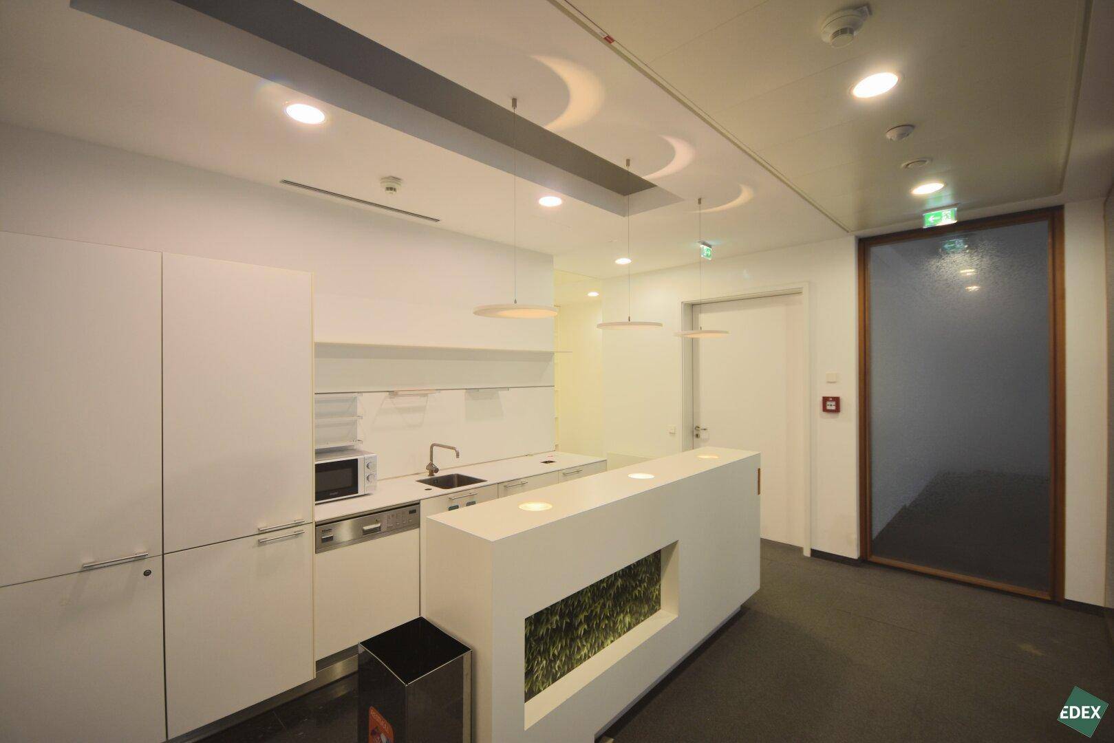 Moderne Teeküche mit weißen Schränken und integrierten Geräten, ideal für Pausen und kleine Mahlzeiten.