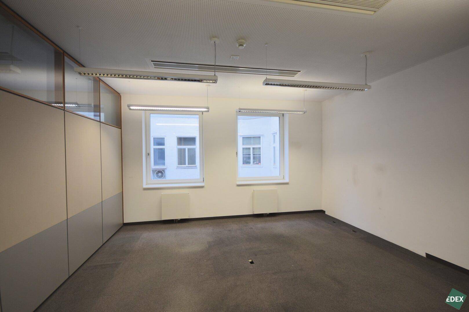 Büro mit Teppichboden und zwei Fenstern, bietet eine ruhige Arbeitsumgebung mit ausreichend Tageslicht.