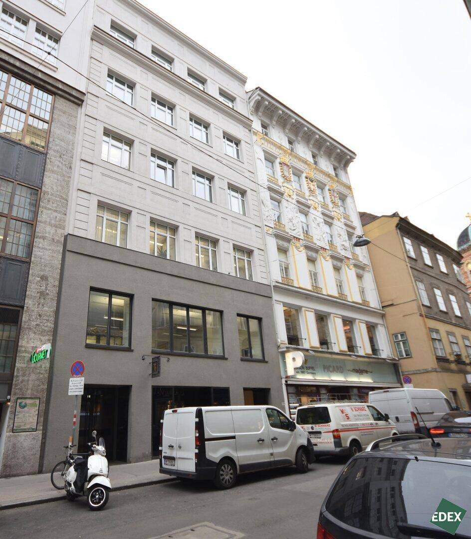 Historisches Gebäude mit moderner Erdgeschossfassade in einer belebten Stadtstraße, umgeben von anderen Gebäuden.
