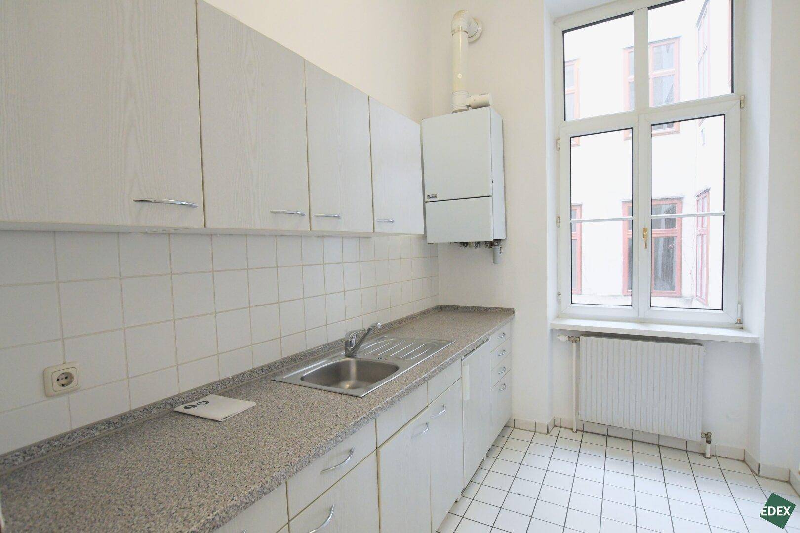 Funktionale Küche mit weißen Hängeschränken, Spüle und Gastherme über der Arbeitsplatte.