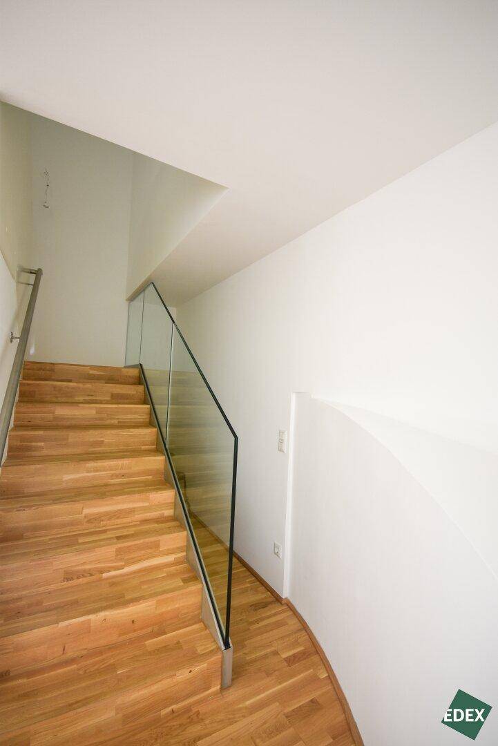 Moderne Holztreppe mit Glasgeländer führt in die obere Etage, hell und offen gestaltet.