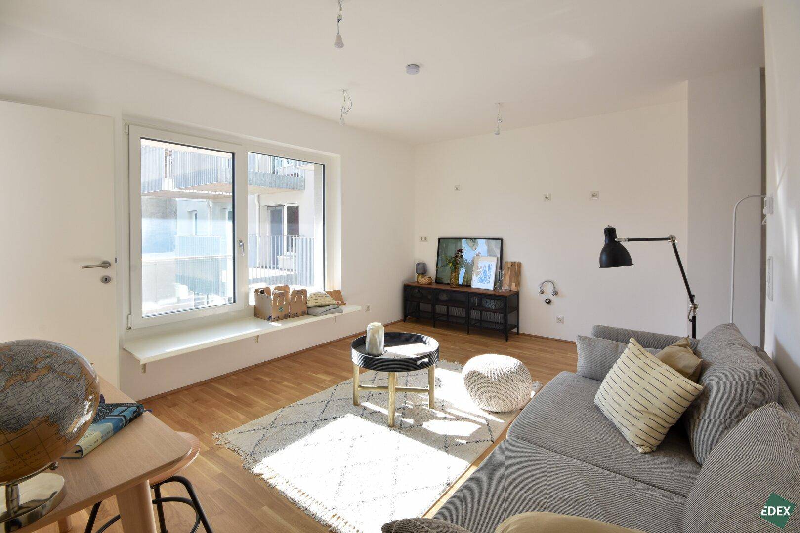 Modernes Wohnzimmer mit Holzboden, großem Fenster und bequemer Couch, hell und einladend.