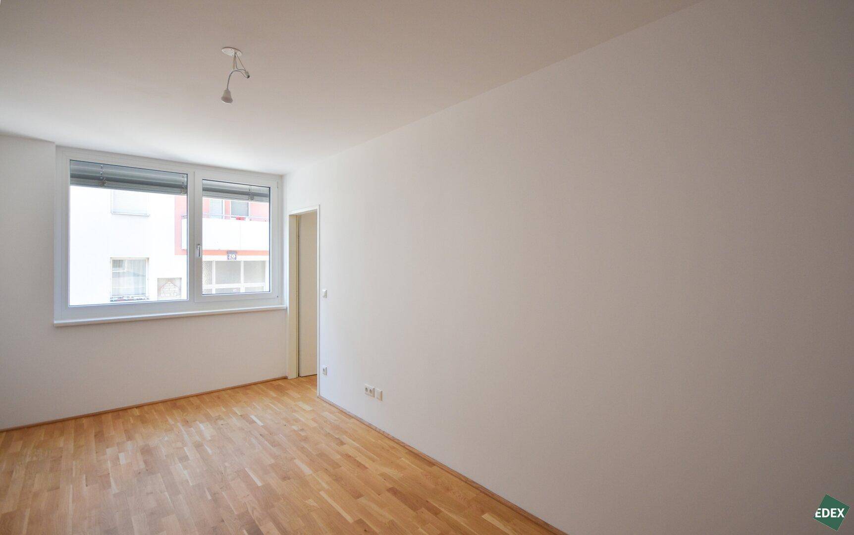Leeres Zimmer mit Parkettboden und großem Fenster, bietet viel Tageslicht und Ausblick.