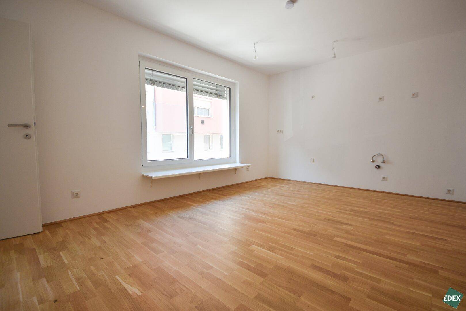 Lichtdurchflutetes Zimmer mit Parkettboden und einem großen Fenster, ideal für Wohnzwecke.