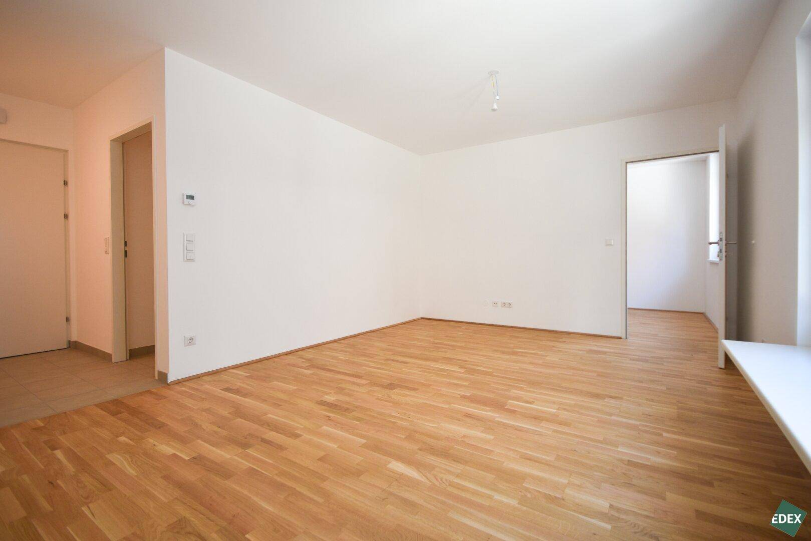 Geräumiges, leeres Zimmer mit hellem Parkettboden und Zugang zu weiteren Räumen.
