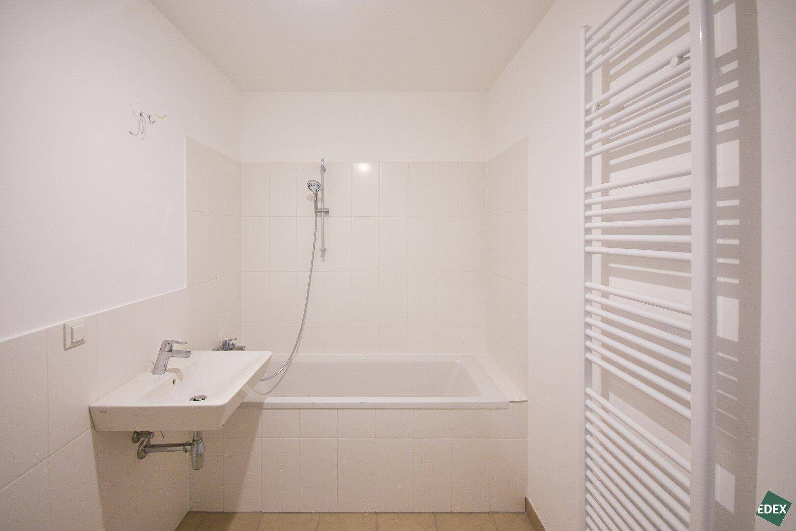 Modernes Badezimmer mit Badewanne, Waschbecken und beheiztem Handtuchhalter, hell gefliest.