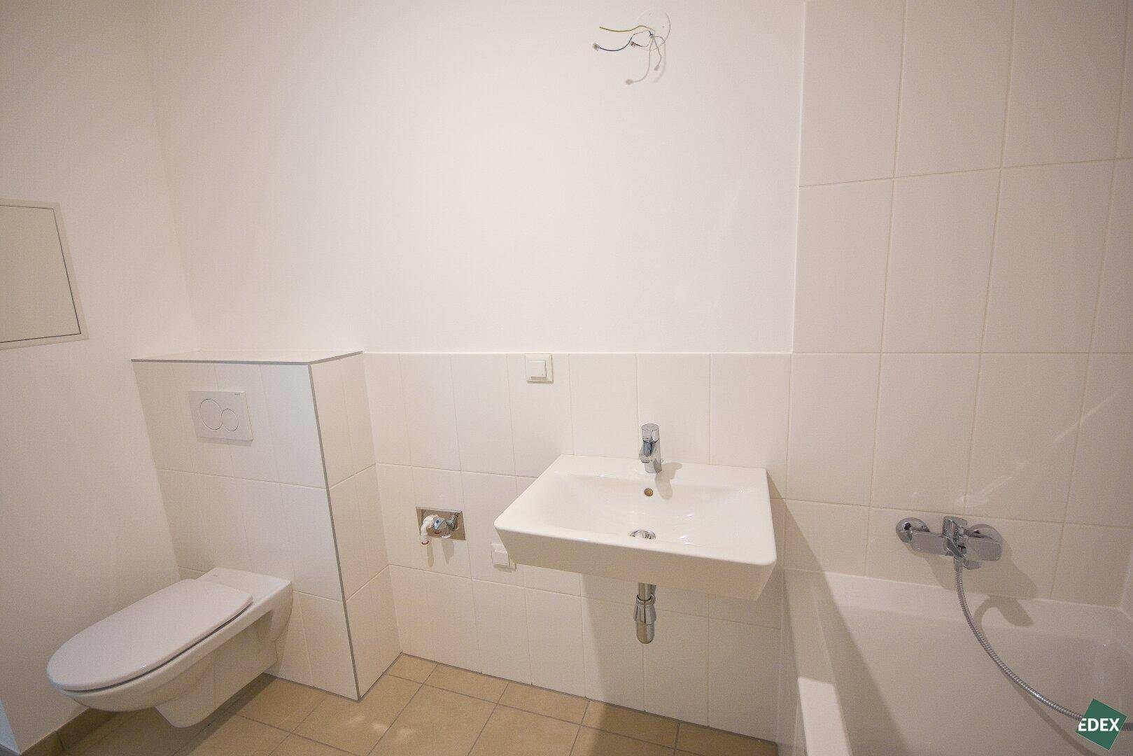 Helles Badezimmer mit Wand-WC, Waschbecken und Badewanne, ausgestattet mit modernen Armaturen.